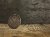 A photograph of an aged coin on its edge, balanced on a rough hewn wooden table