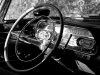 A black and white photograph of the interior of a vintage Cadillac with the focus on the steering column and gauges