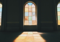 A photograph of a stained glass window from inside a darkened room with the color and light through the window projecting on to the floor