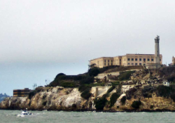 A prison sits atop an island. A boat rides in the waters at the island's feet
