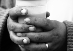 A black and white photograph of a pair of hands grasping a plastic coffee cup