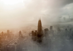 A digital altered photograph of Kuala Lumpur shrouded in fog or smog with greys and browns mixed into the haze