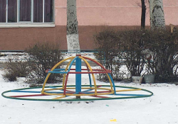 A photograph of a multi-colored merry go round on the snowy ground outside of a school