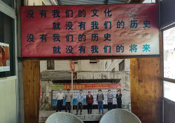 A photograph of several people standing in a row is mounted on a wall, beneath a banner adorned with Chinese characters