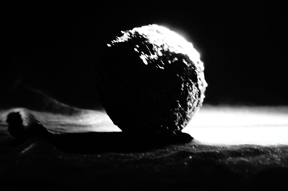 A black and white photo of a ball of aluminum foil, mostly in darkness but lit up on one side by a focused light