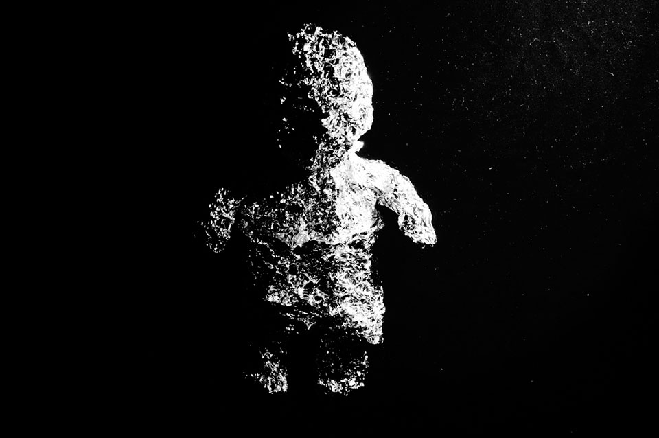 A black and white photo of a small human figure made of aluminum foil that is brightly lit on its right side