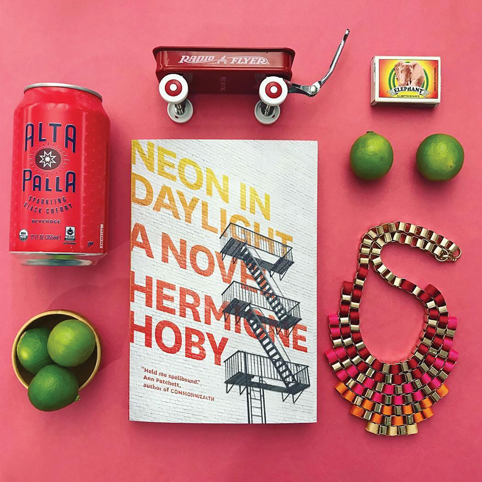 An Instagram style photo of a book surrounded by other objects on a flat pink background