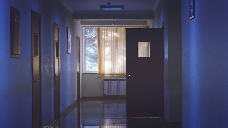 A hallway in a hospital with an door open just before a window lit by the sun