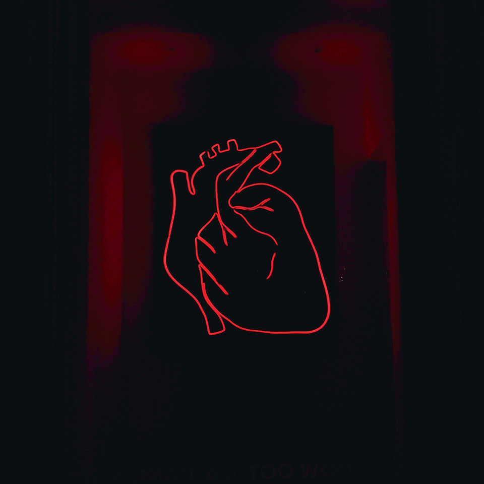 The red neon outline of a heart sits on a black background with crimson frames surrounding the heart
