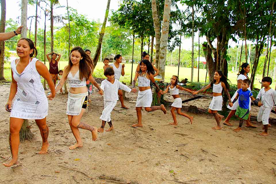 Children, dressed in white, dance in a line while holding hands