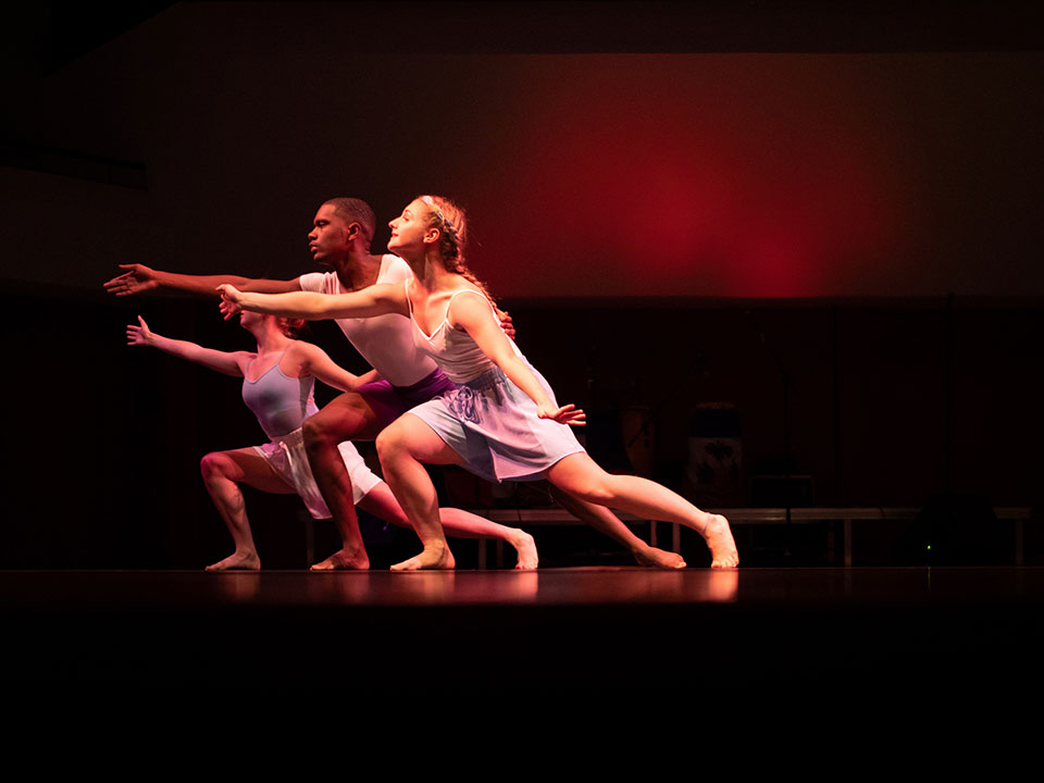 Three dancers lunging to the left, with a dark red background