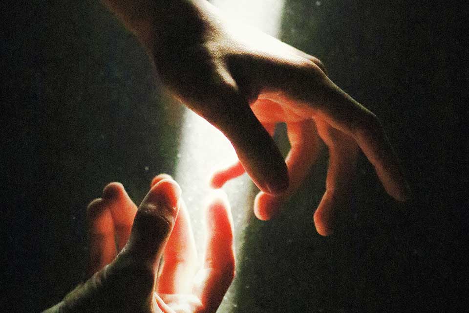 A pair of hands in a dark space illuminated by light from above
