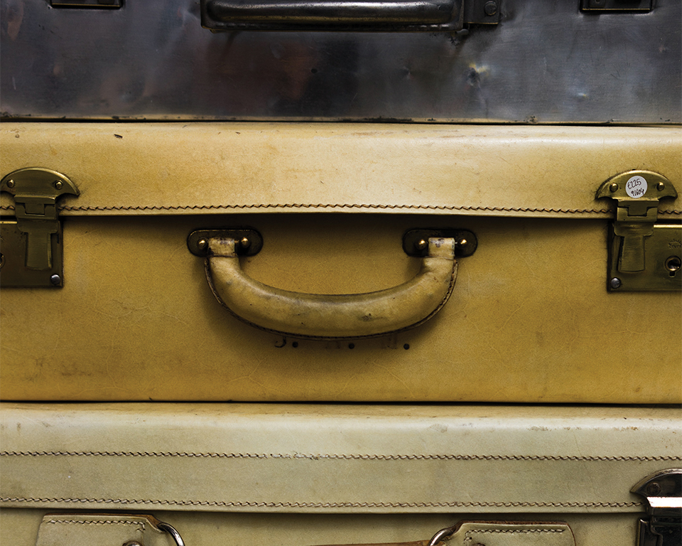 A close up photograph of three aged suitcases stacked flat on one another