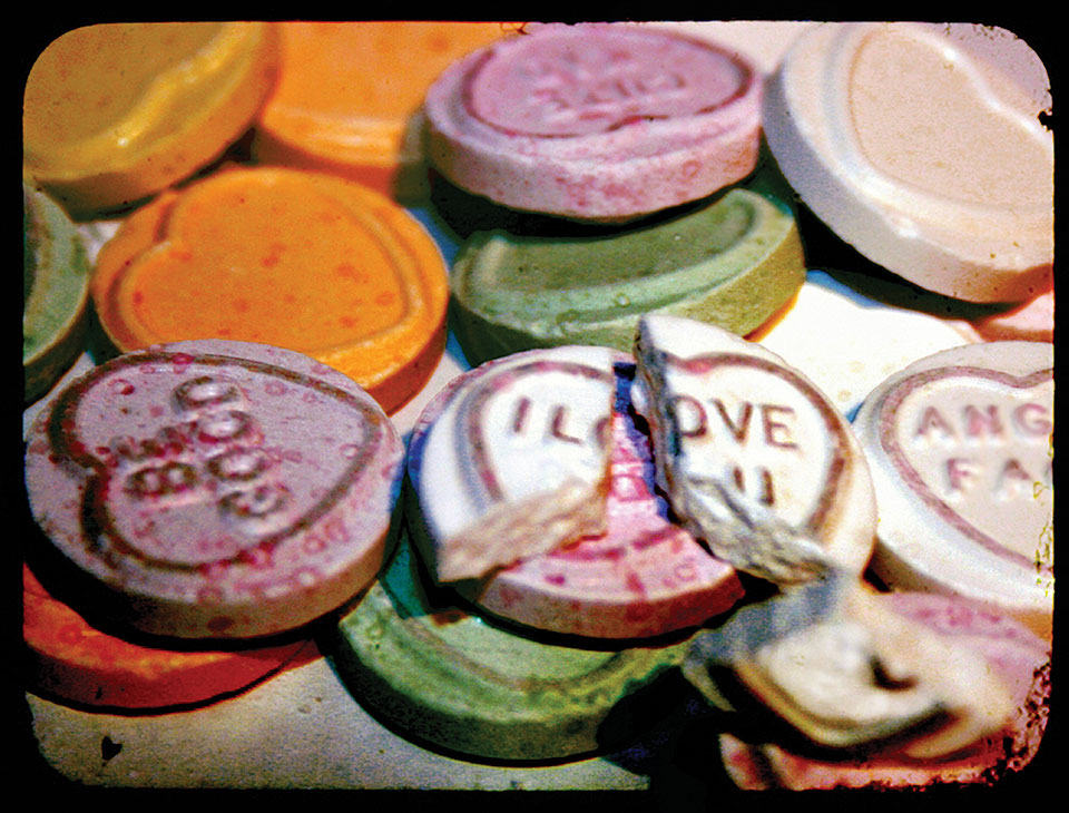 A pile of conversation hearts with one that reads "I Love You" broken at the top of the pile