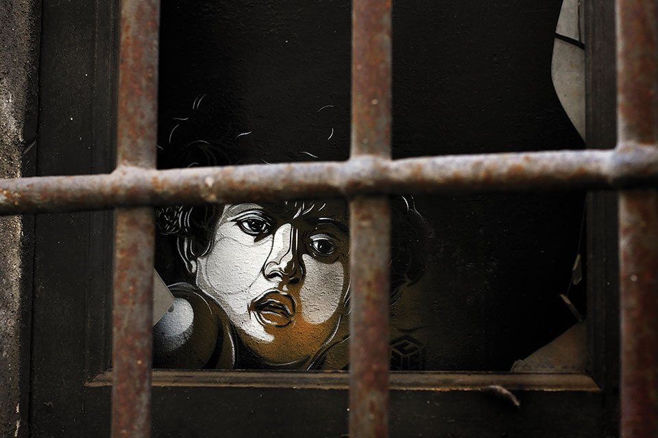 The drawn image of a human face peers from within a darkened room through iron bars