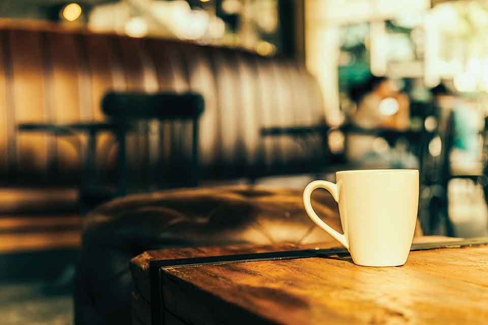 A photograph of a mug on a wooden table. A coffee shop can be seen out of focus in the background