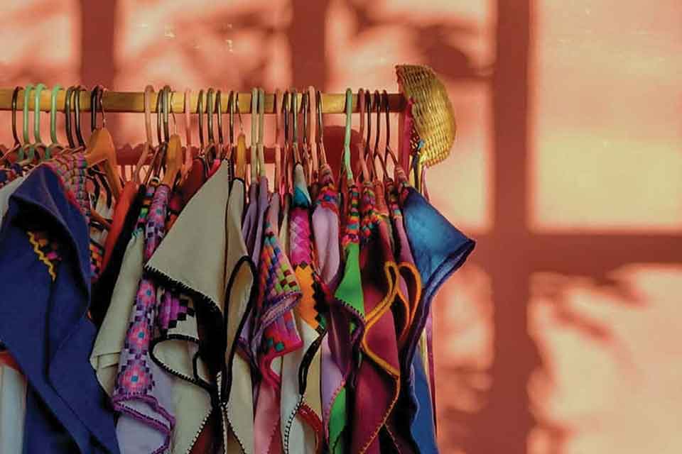 A photograph of a rack of brightly colored clothing on hangers