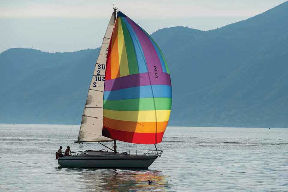 A sailboat with a rainbow sail on a lake