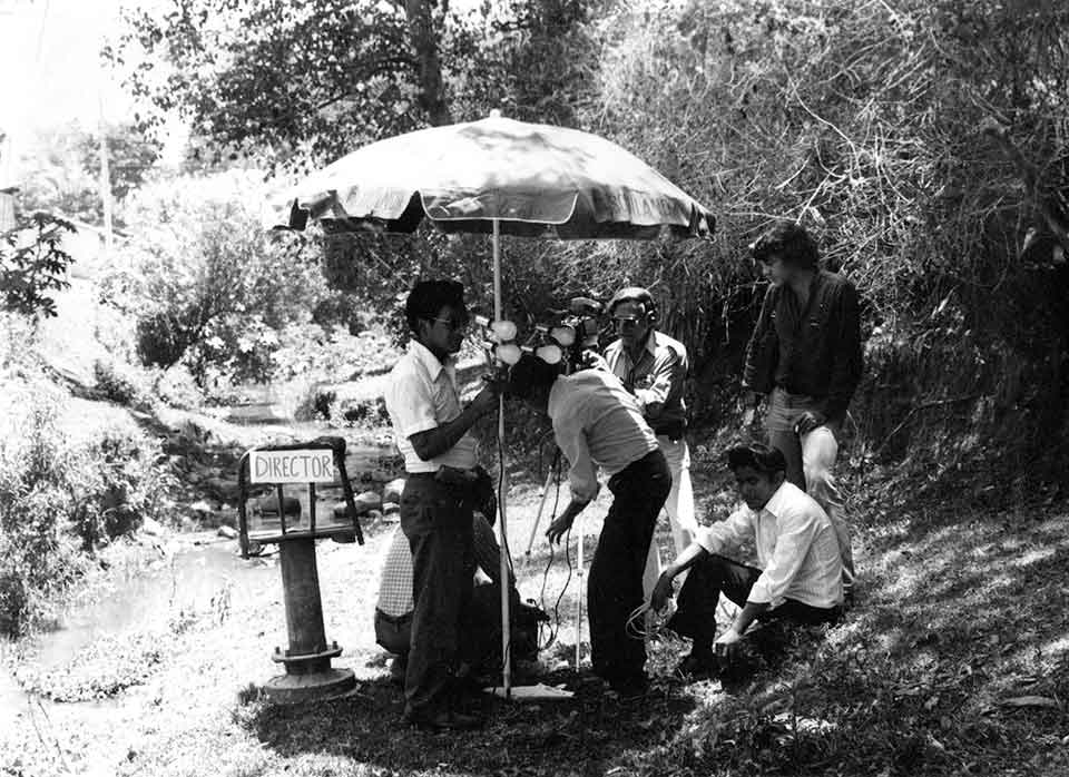 A black and white photograph of men working to secure an umbrella on a film set located in a jungle