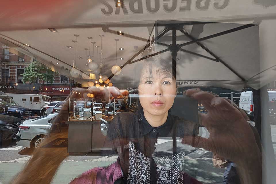 A photograph of a woman appearing in the reflection of a shop window
