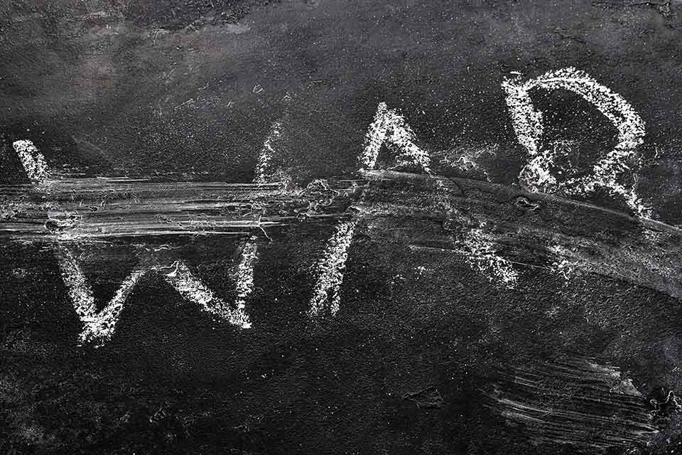 A black and white photograph of the word war written in chalk on a black background. The word is being blown away