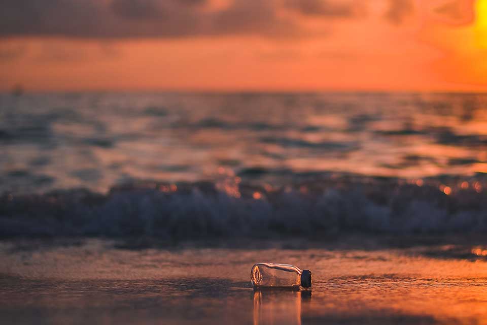A photograph of a bottle overturned on a beach at sunset
