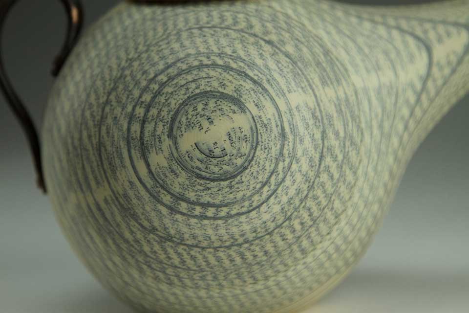 A detail of a photograph of a tea pot, focusing on a spiral on its belly