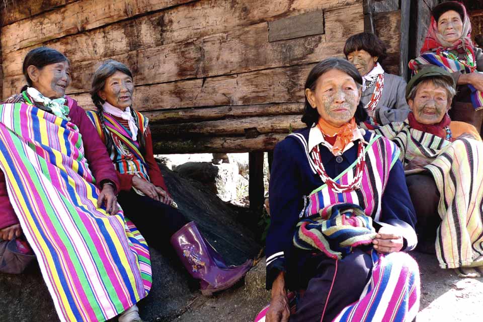 A small clutch of elderly women with face tattoos, garbed in native dress