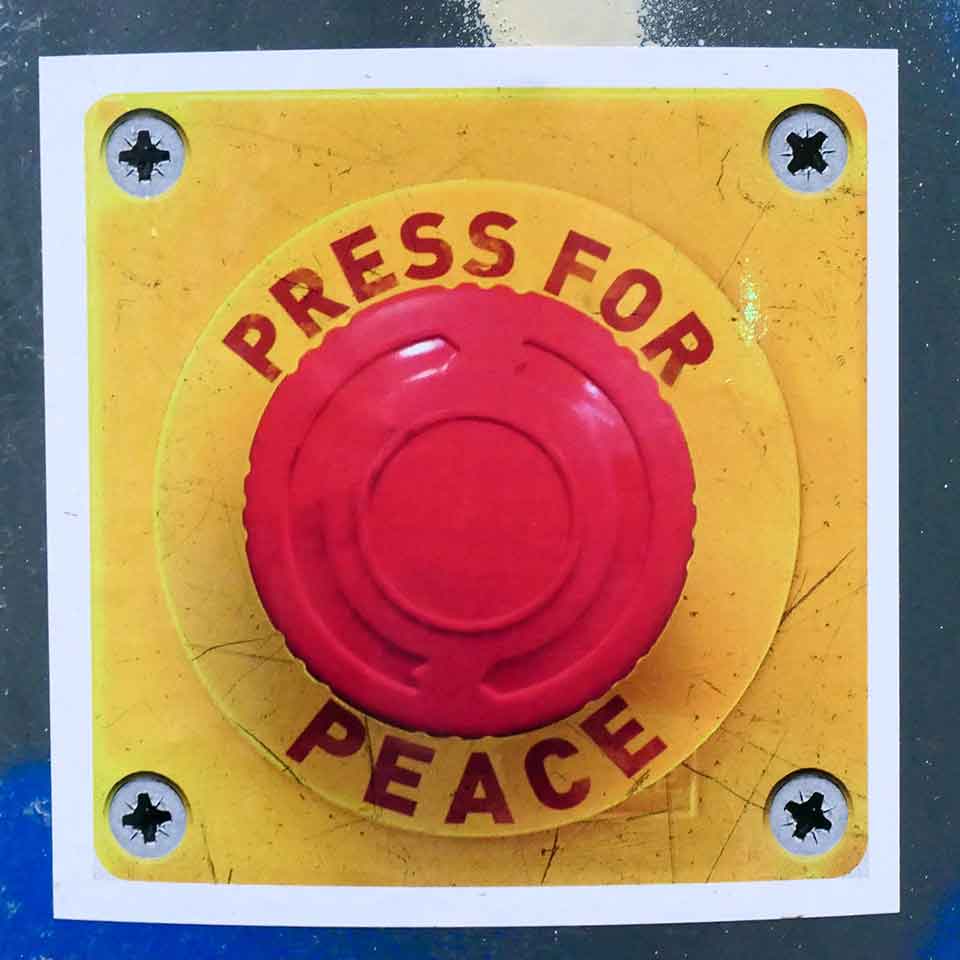 A red button mounted on a yellow background. Text arounds the buttons reads: Press for Peace
