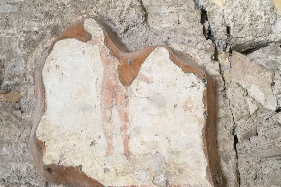 A photograph of a broken piece of mosaic depicting the bottom half of a human figure