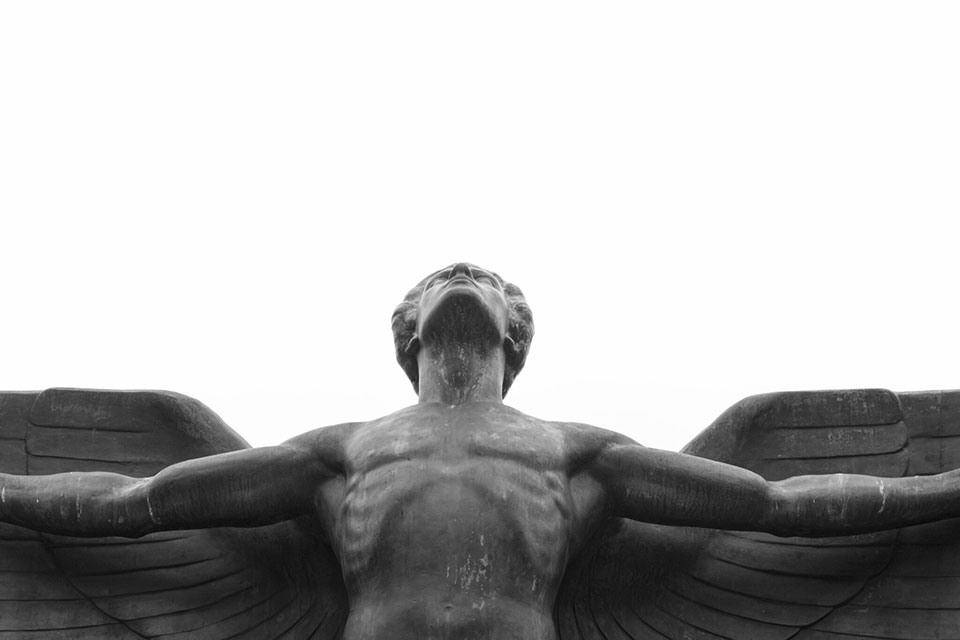 A photograph of a winged figure looking upward into a perfectly white sky