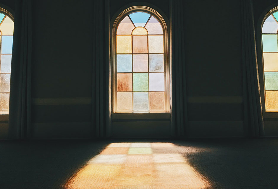 A photograph of a stained glass window from inside a darkened room with the color and light through the window projecting on to the floor