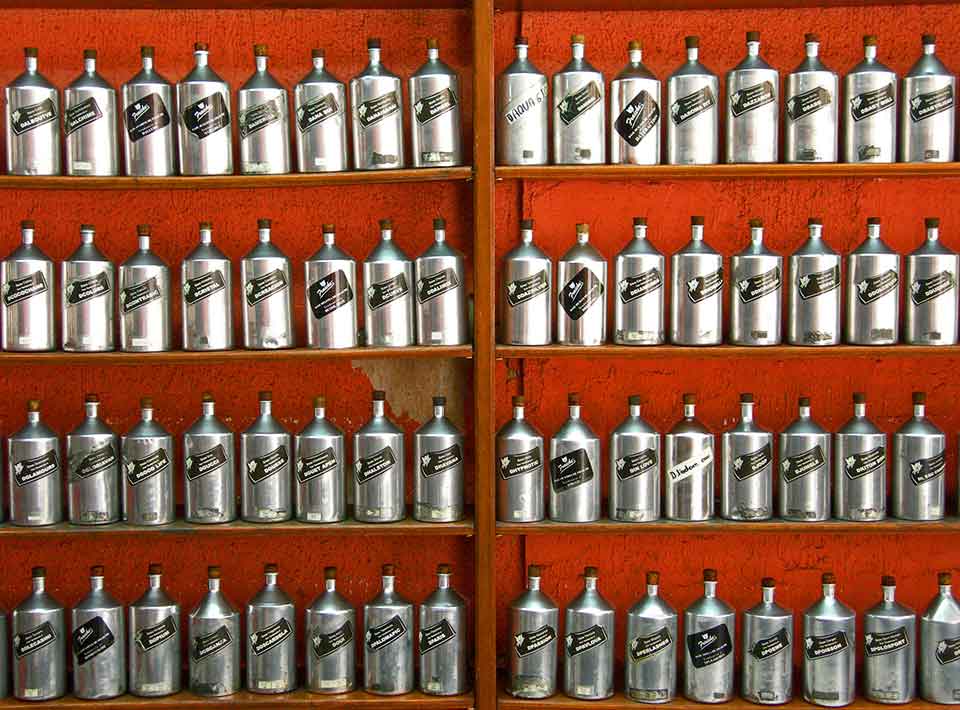 A photograph of long rows of hair tonic in metallic bottles against a red-orange wall