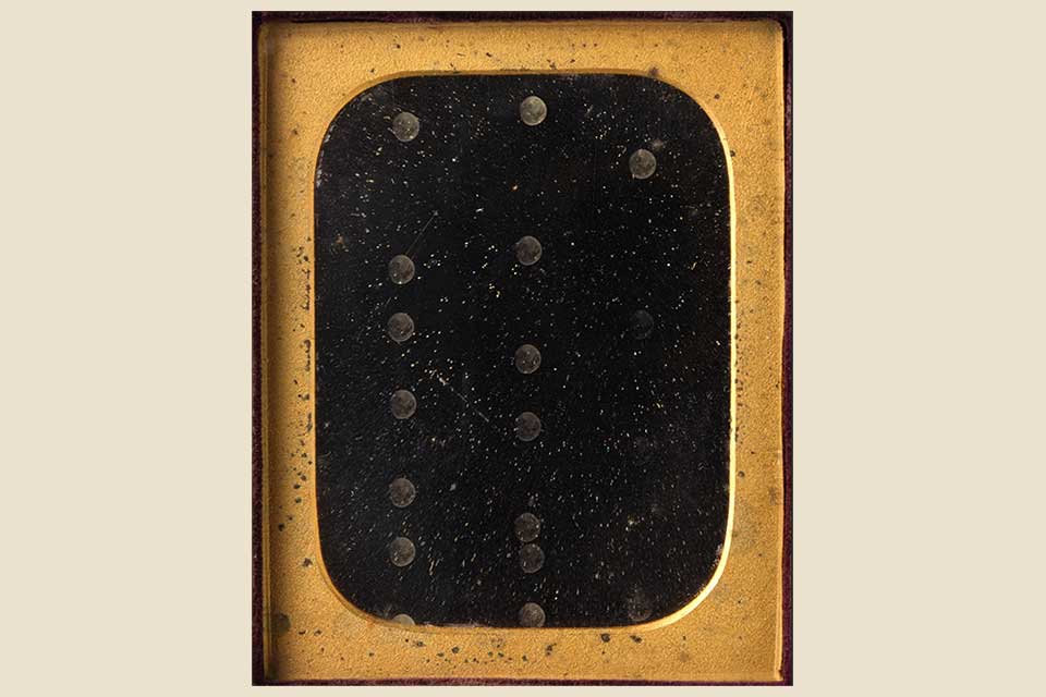An abstract image of a black field with circles embossed into it, framed by gold. The image is set against a cream background.