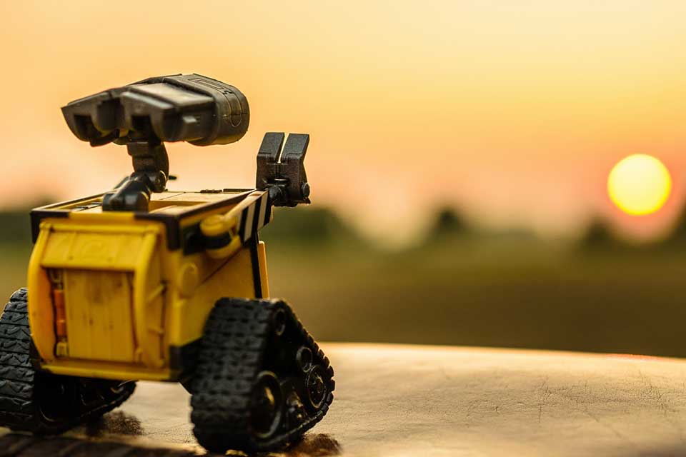 A photograph of a toy robot with a setting sun in the background