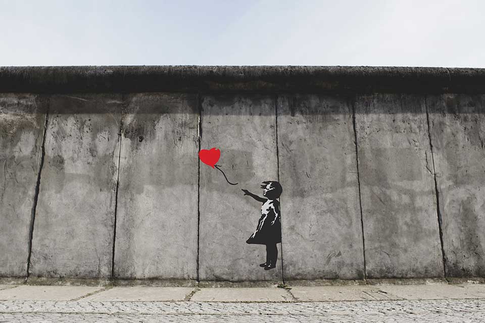 A painting of a girl in black and white holding a red balloon on a drab gray wall