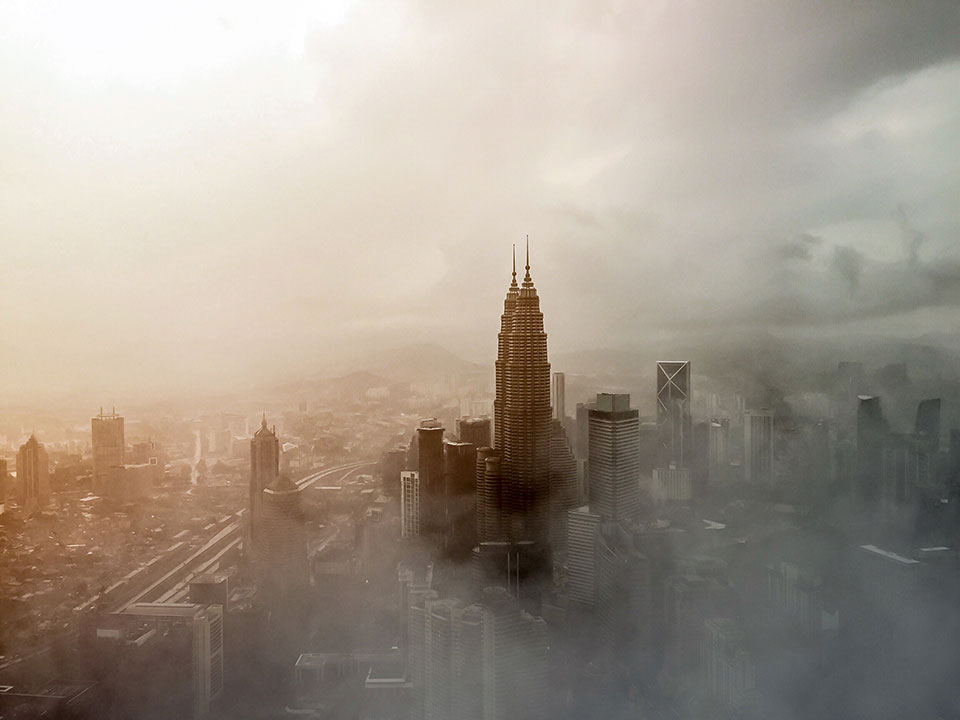 A digital altered photograph of Kuala Lumpur shrouded in fog or smog with greys and browns mixed into the haze