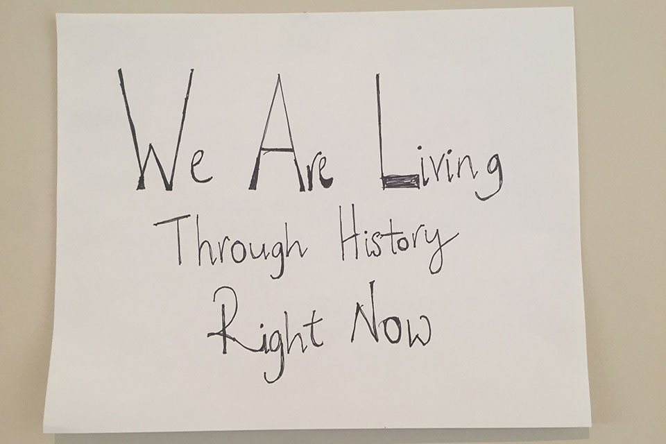 A hand-written sign. Text reads: We are living through history right now.