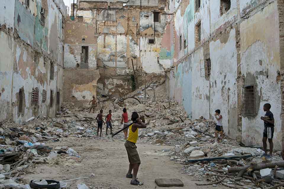 A group of boys play stickball in an urban cul-de-sac filling up with piles of rubble