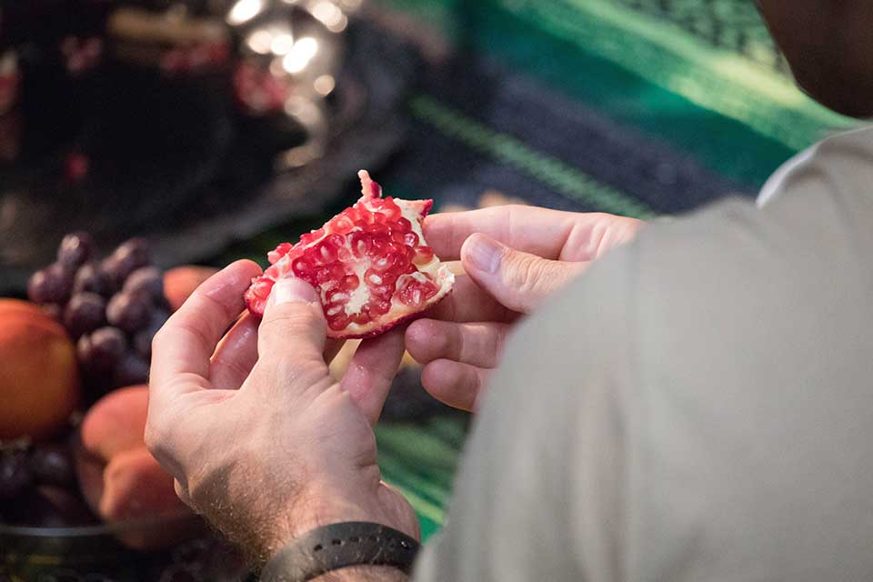 A photograph taken over a man's shoulder as he opens a pomegranate.