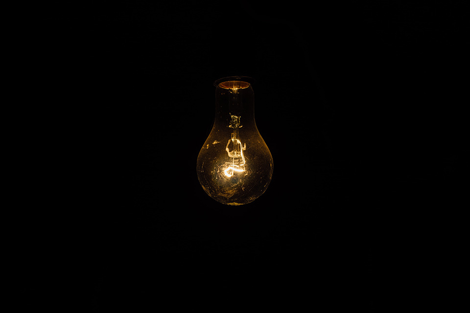 A photograph of a very dim lightbulb that is all but being swallowed by the darkness surrounding