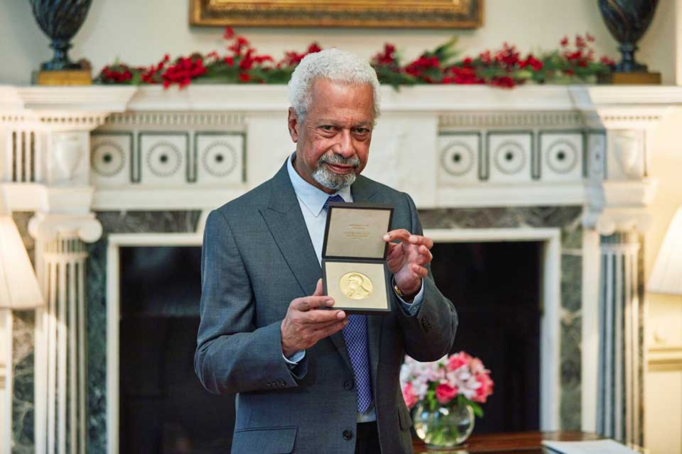 A photograph of Abdulrazak Gurnah holding up his recently awarded medal from the Nobel committee