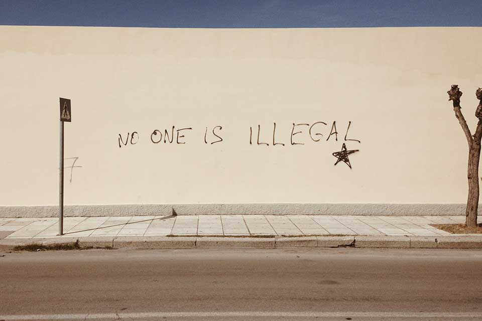 A photograph of a wall with the words, "No one is illegal" spray painted on it
