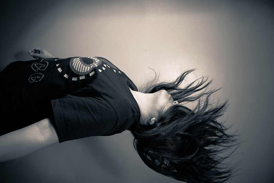 A black and white photograph of a woman in a t-shirt. It has been rotated such that it appears as if she is floating, weightless