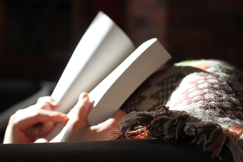 Person reading a book with blanket and sunlight