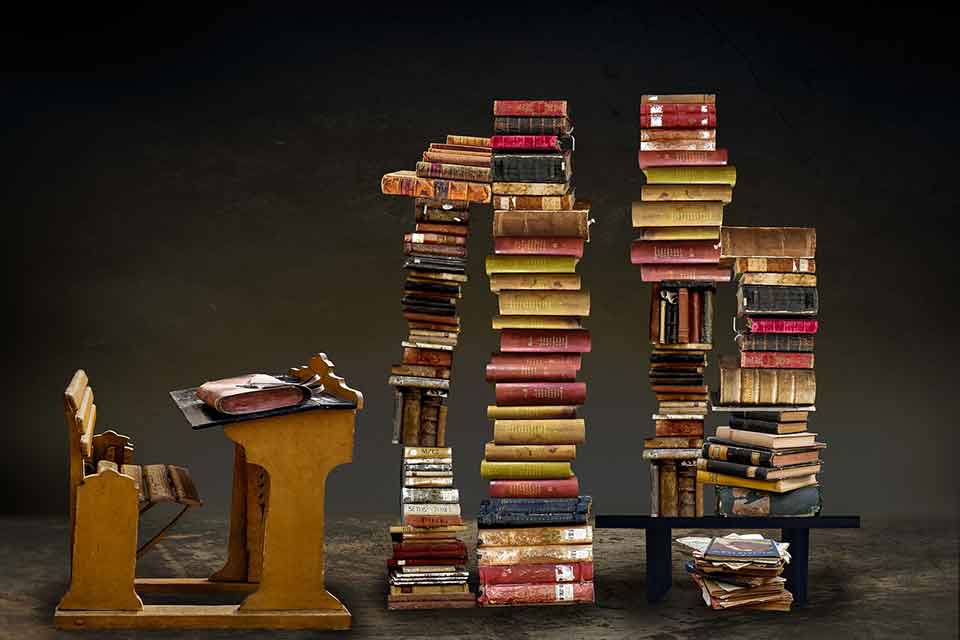 A photo of an antique student desk facing several stylishly designed stacks of books