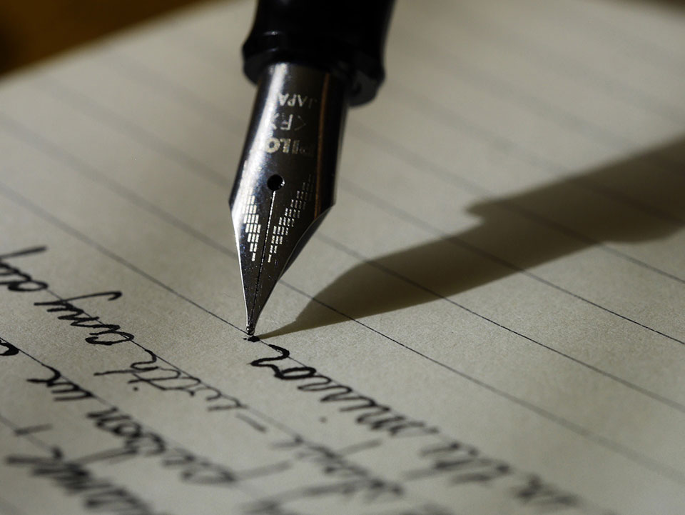 An old-style fountain pen writes on lined paper.