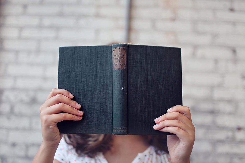 Woman holding a hardback book in front of her face.