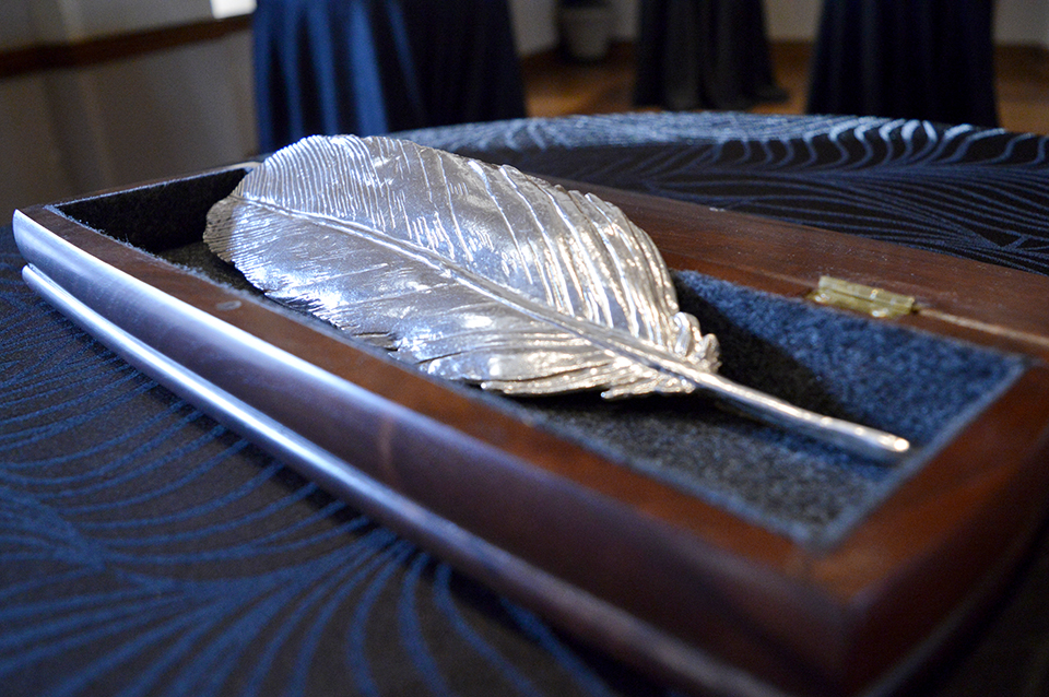A feather, cast in silver, rests in a velvet lined box