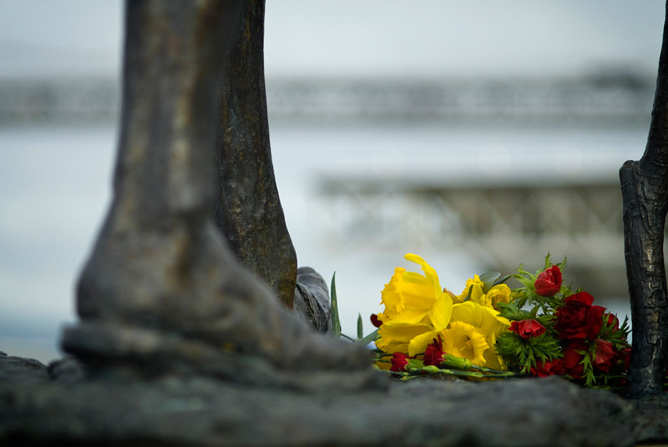 A close-up of a human foot in statue form with flowers laid before it